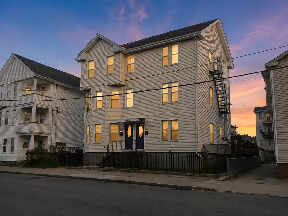 Two white houses on a street at dusk, with lit windows and a pink-blue sunset sky.