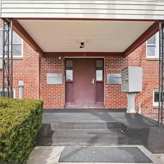 Brick apartment entrance with maroon double doors, steps, and a covered porch.