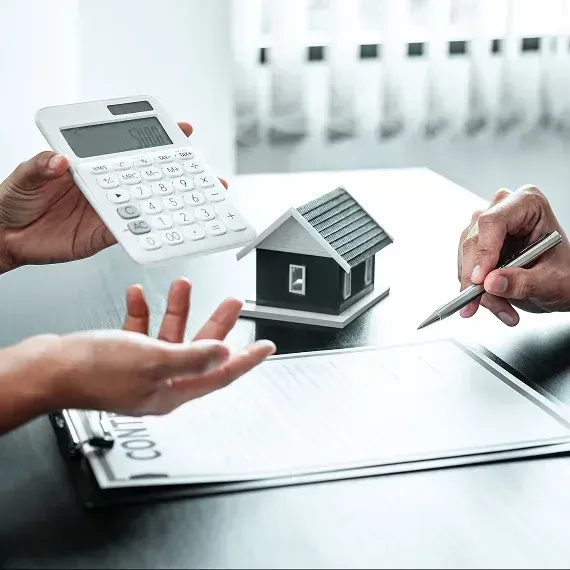 Hands, calculator, house model, and pen over a mortgage document on a desk