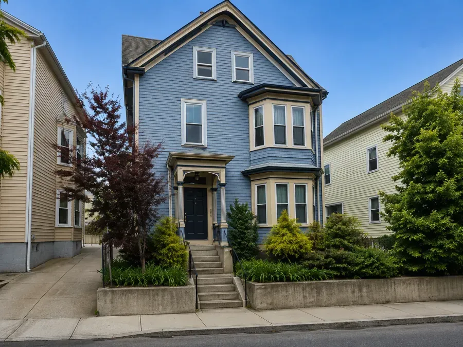Blue two-story house with bay windows, front steps, and small front yard on a residential street