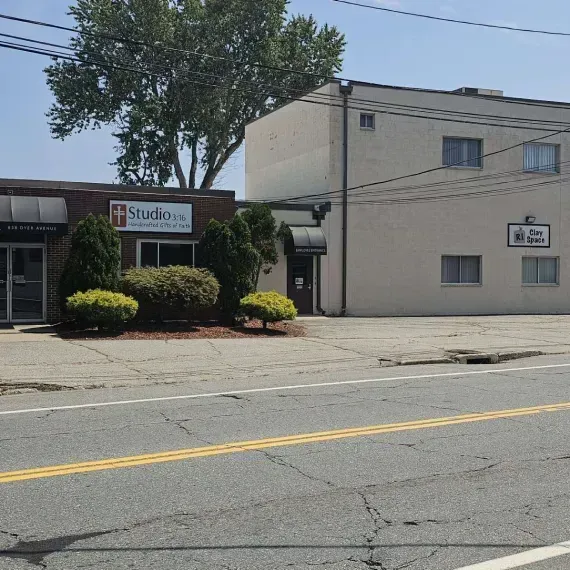 Street view of a studio building and adjacent beige office, with trees and road in front.