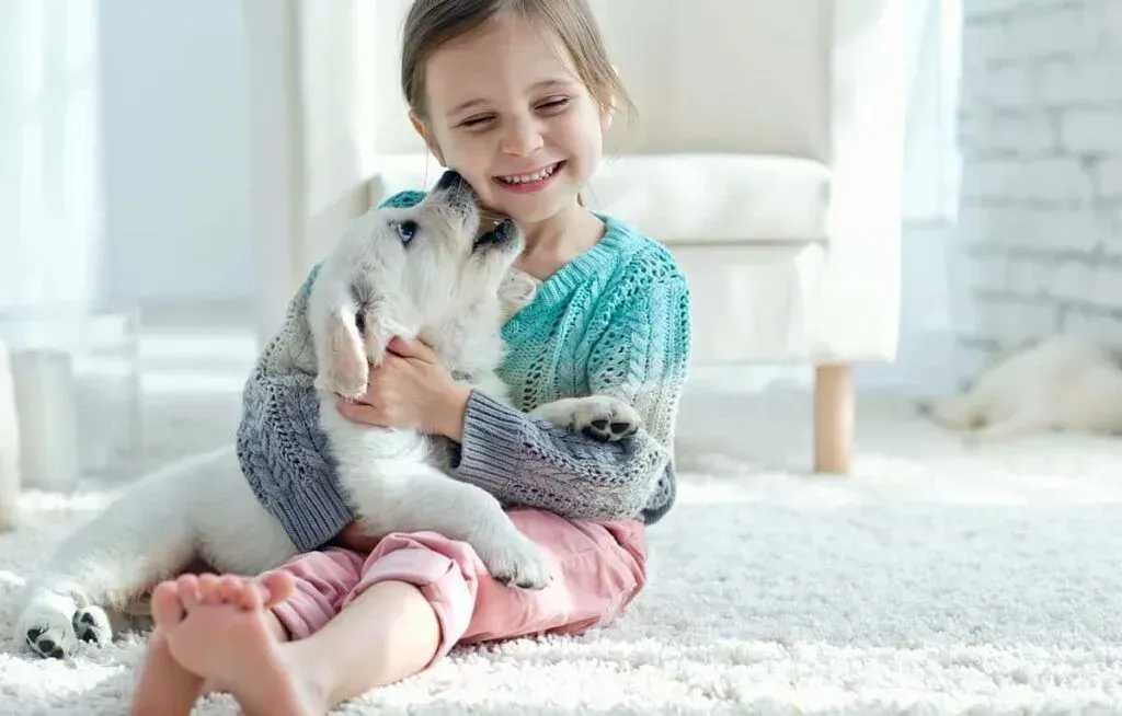 A little girl is sitting on the floor holding a puppy.