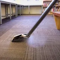 A vacuum cleaner is cleaning a carpeted floor in a library.