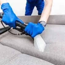 A person is cleaning a couch with a vacuum cleaner.