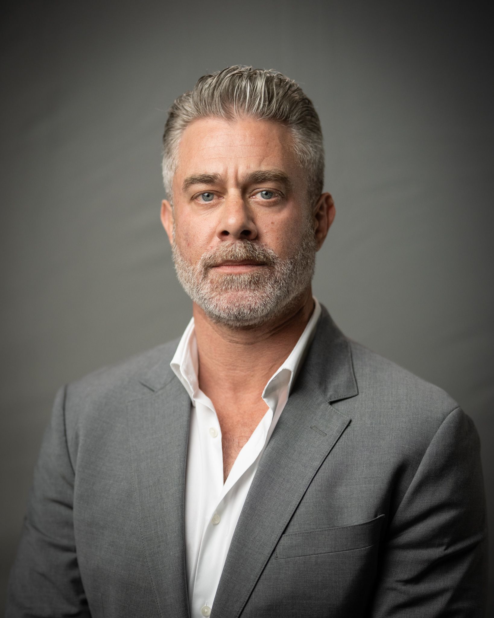 Studio portrait of a man in a gray blazer and white shirt against a dark background