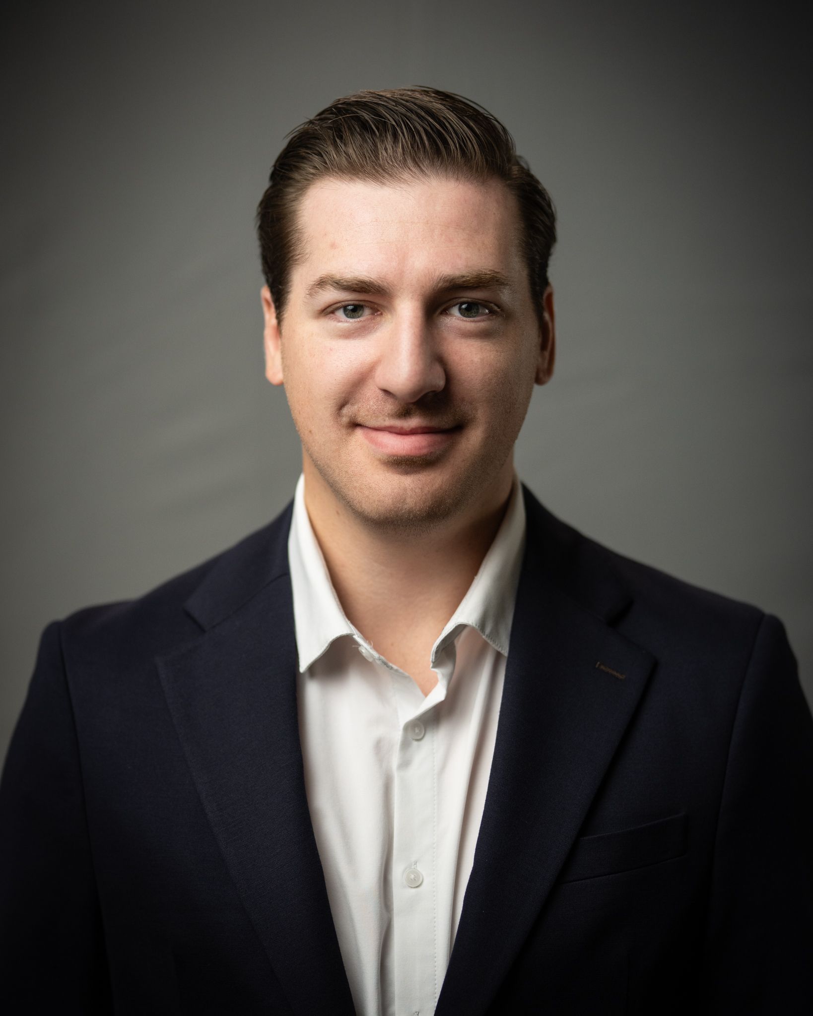 Studio portrait of a man in a dark suit and white shirt against a gray background