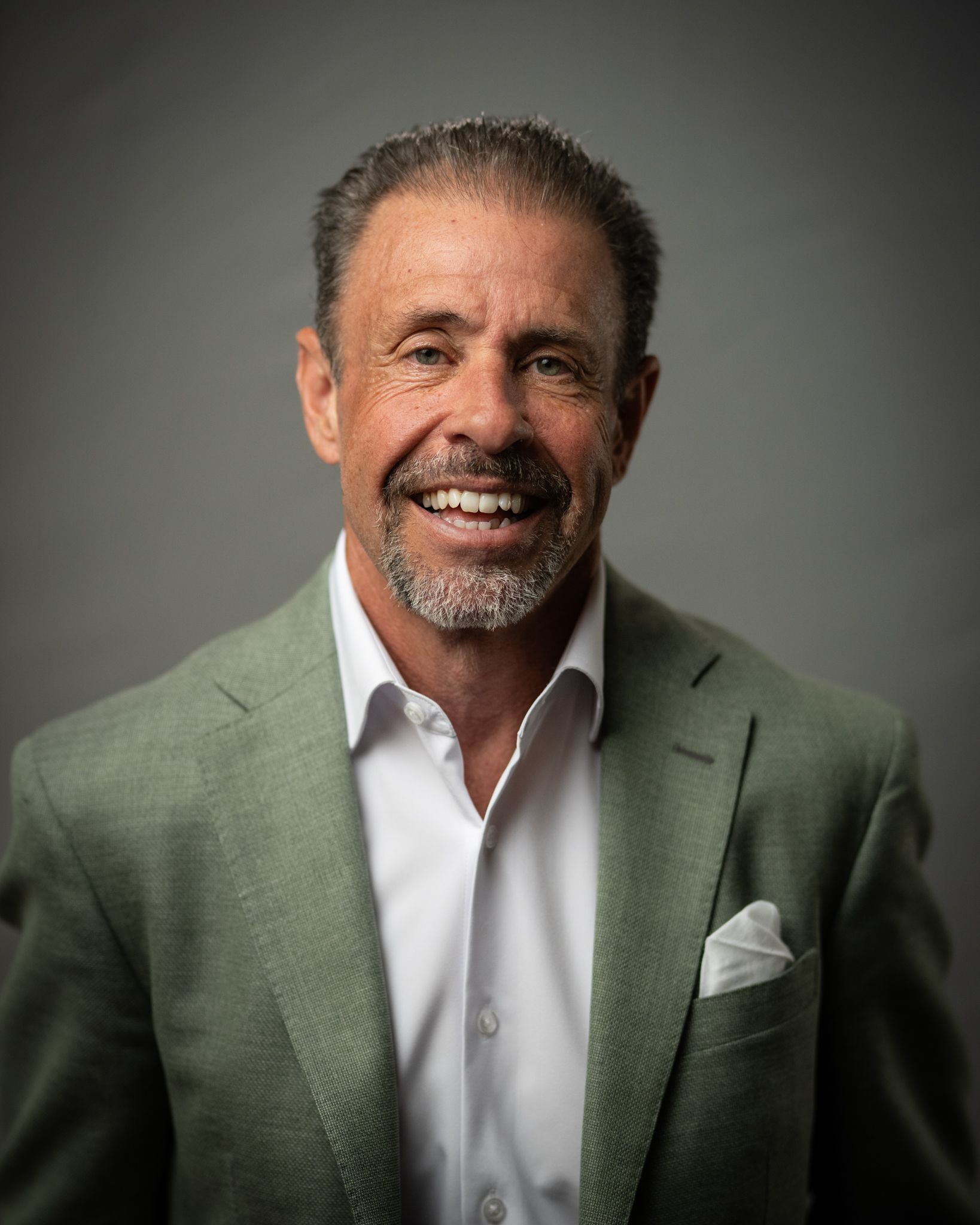 Man in a plaid blazer and white shirt smiling in front of a blurred bookshelf background