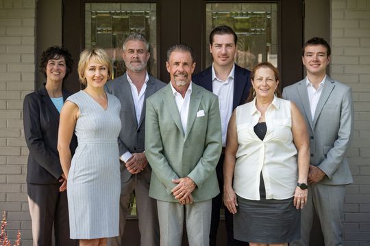 Six people standing together outside a building, dressed in business attire, posing for a group photo
