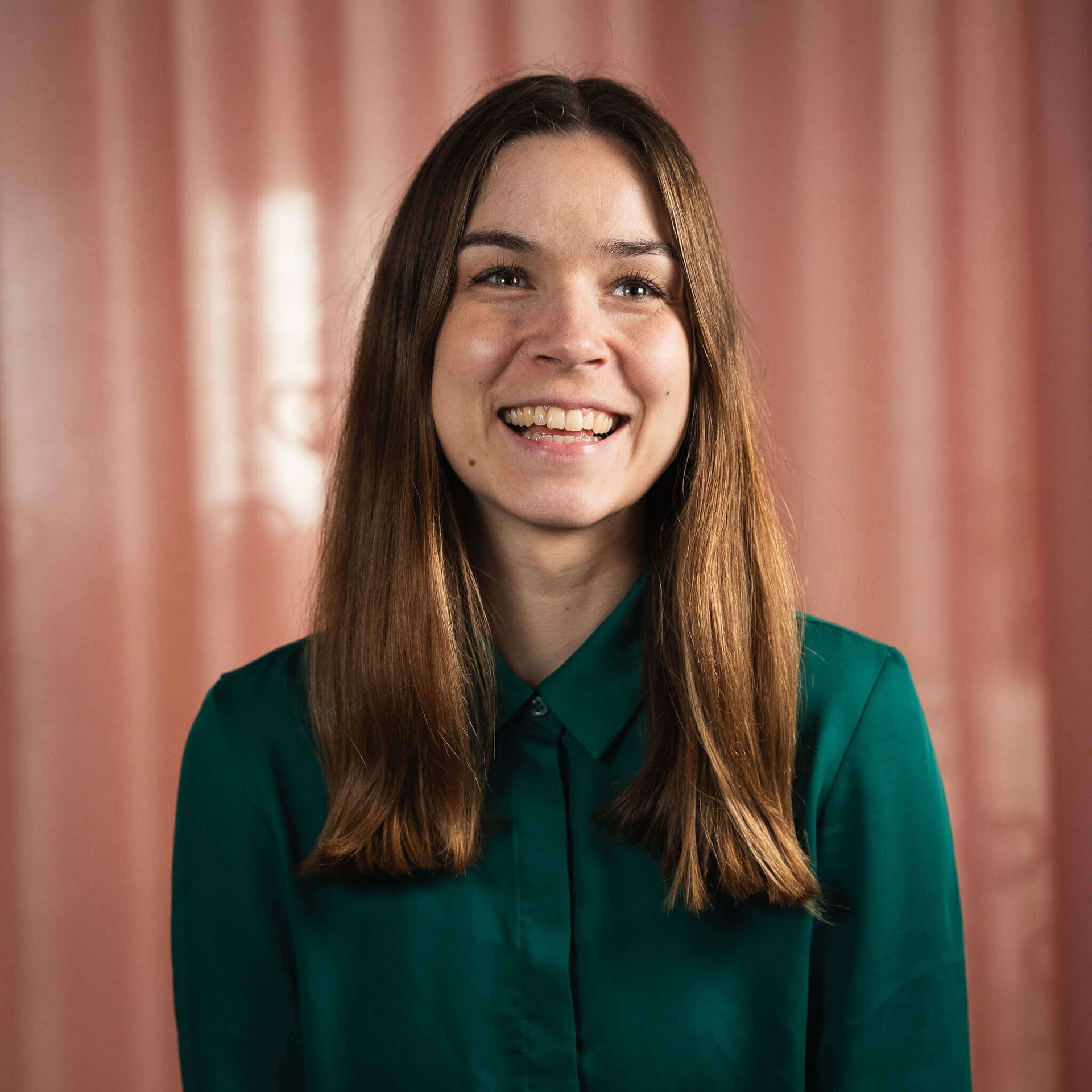 Een vrouw in een groen shirt lacht voor een roze gordijn.