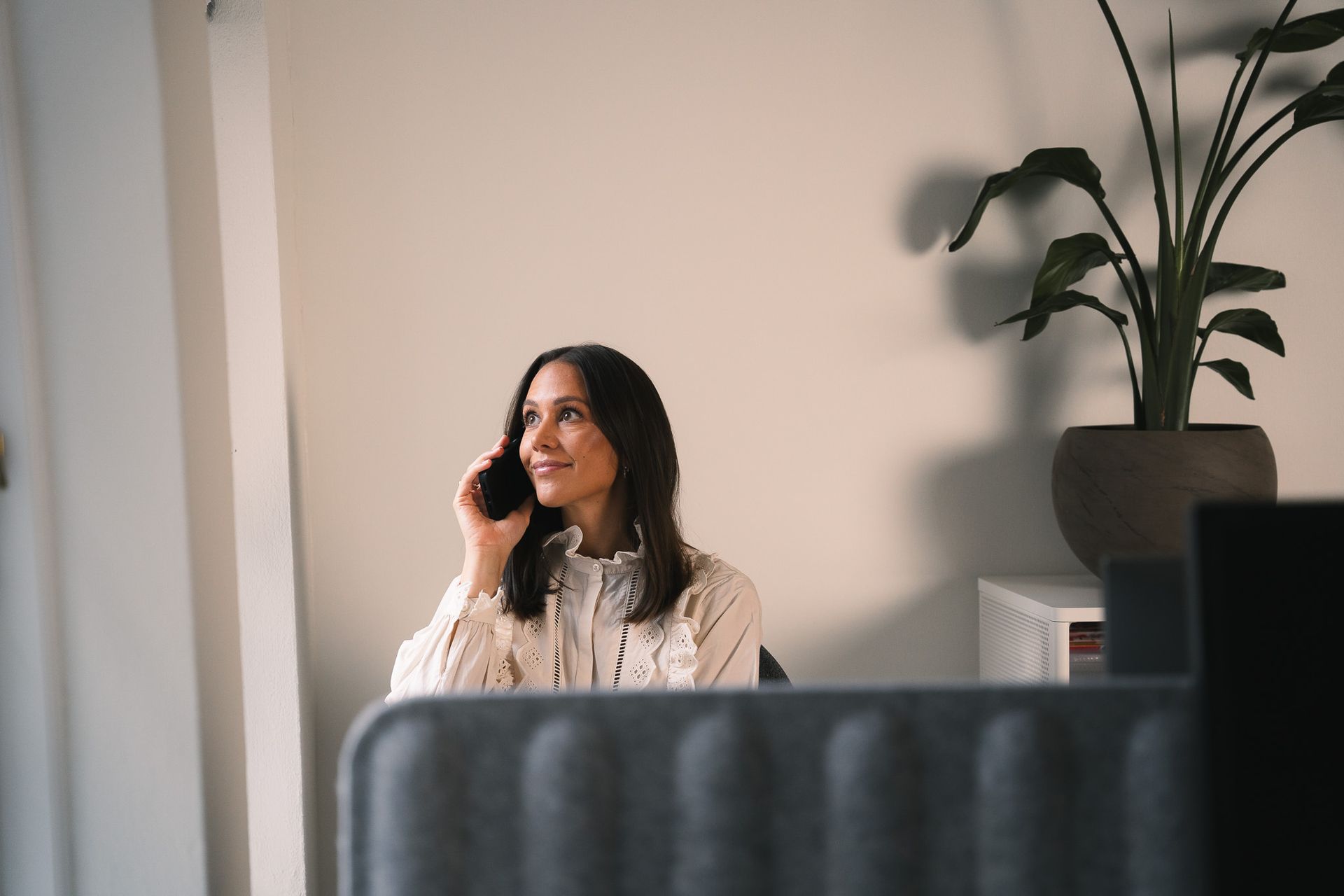 Een vrouw zit aan een bureau en belt via een mobiele telefoon.