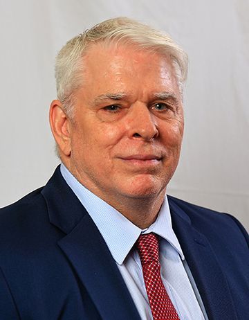 Headshot of a man with light gray hair wearing a blue suit, light blue dress shirt, and a red patterned tie.