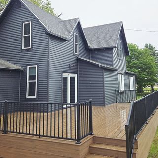 Three workers on a roof covered in bright blue underlayment, with ladders positioned against the siding of the house.