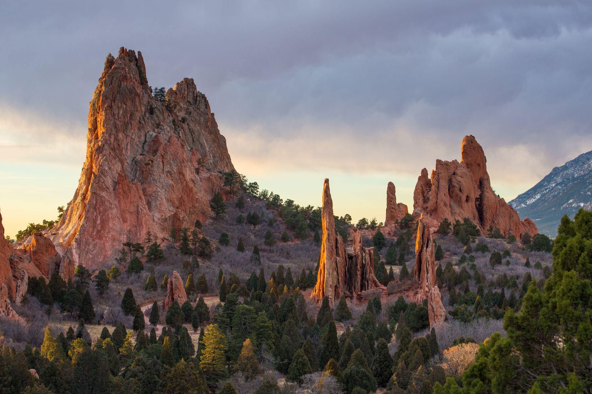 Sunset-lit jagged rock spires above a forested mountain landscape under a cloudy sky