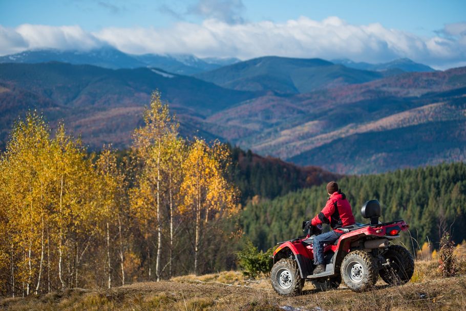 Person riding a red ATV through an autumn mountain landscape with yellow trees and distant peaks