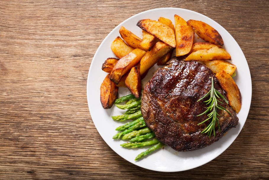 Grilled steak with potato wedges and asparagus on a white plate on a wooden table