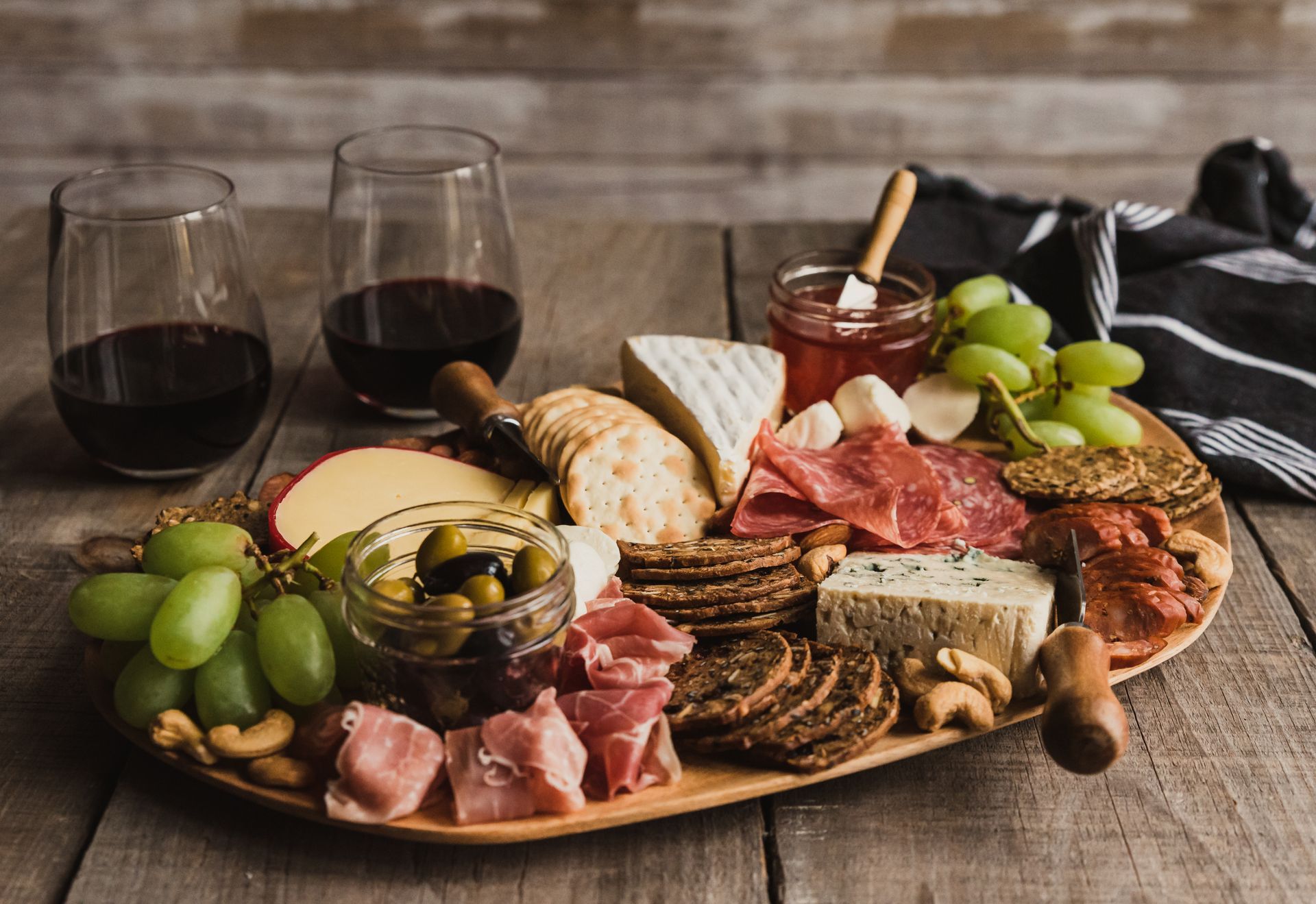 Charcuterie board with meats, cheese, grapes, crackers, olives, and two glasses of red wine on a rustic table