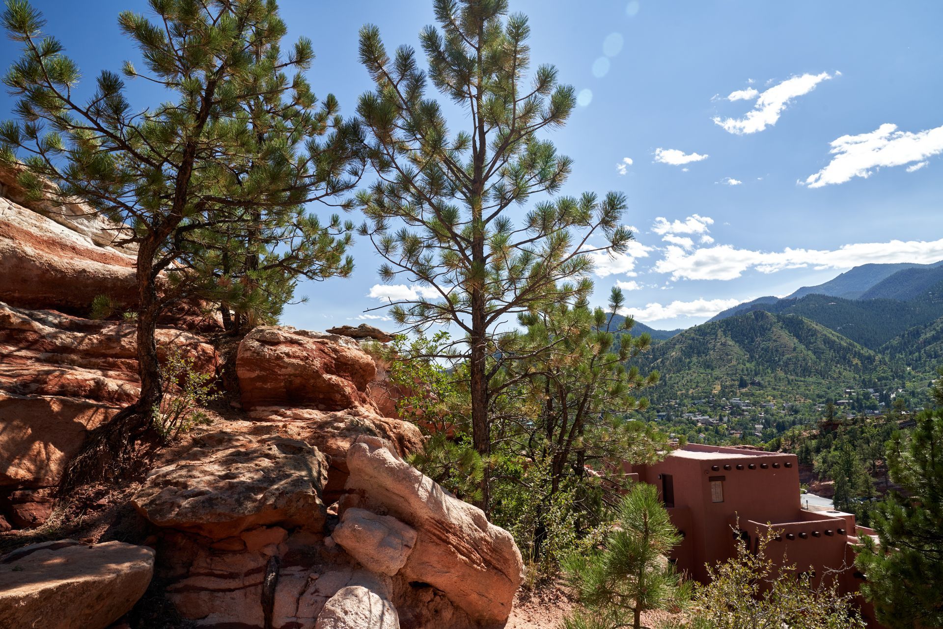 Red rock canyon with pine trees, blue sky, and a small building in the foreground