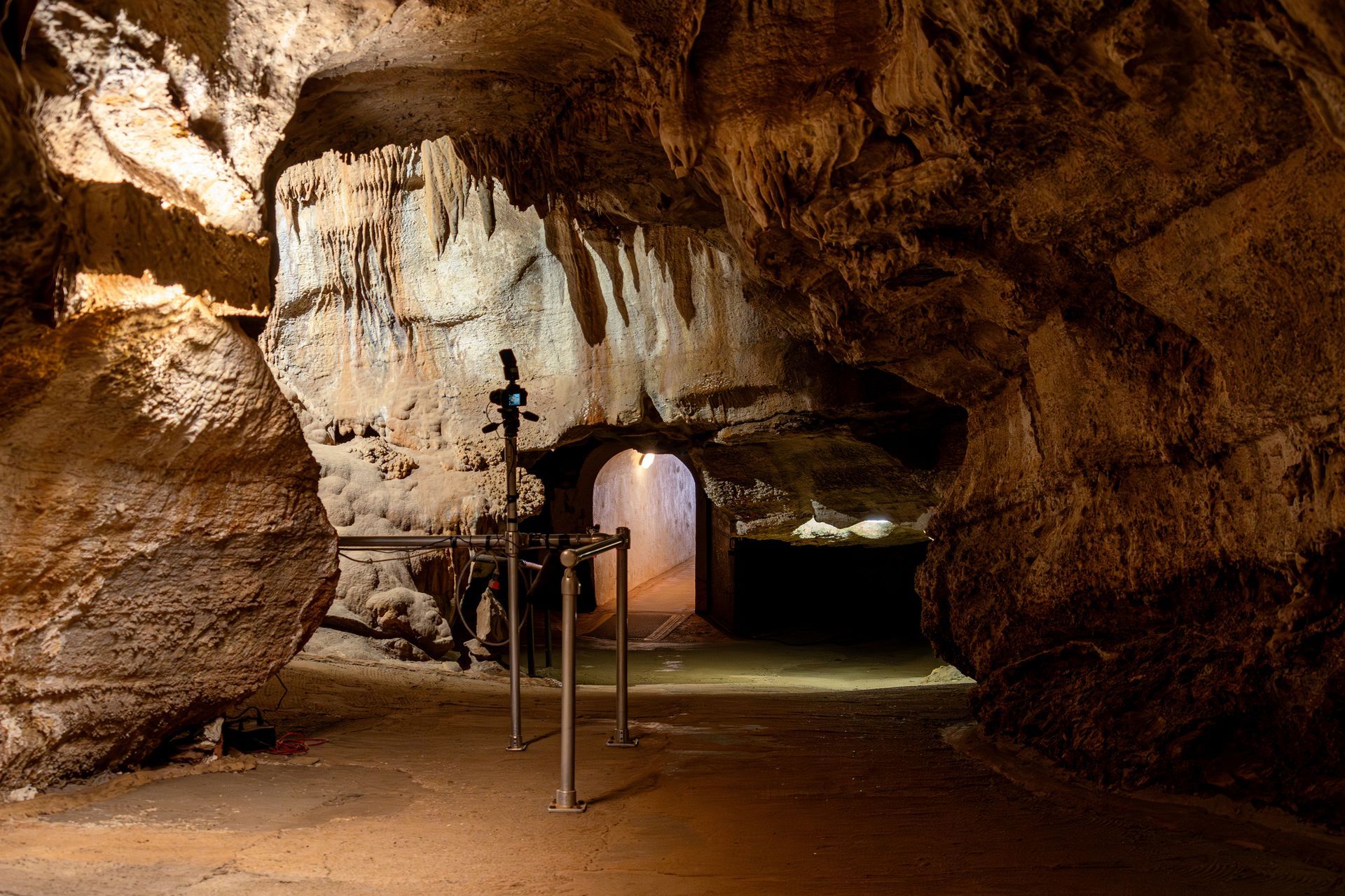 Rocky cave interior with a lit doorway and metal railing pathway