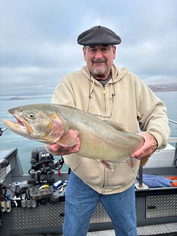 Man holding large fish on a boat; cloudy day, neutral tones, happy expression.