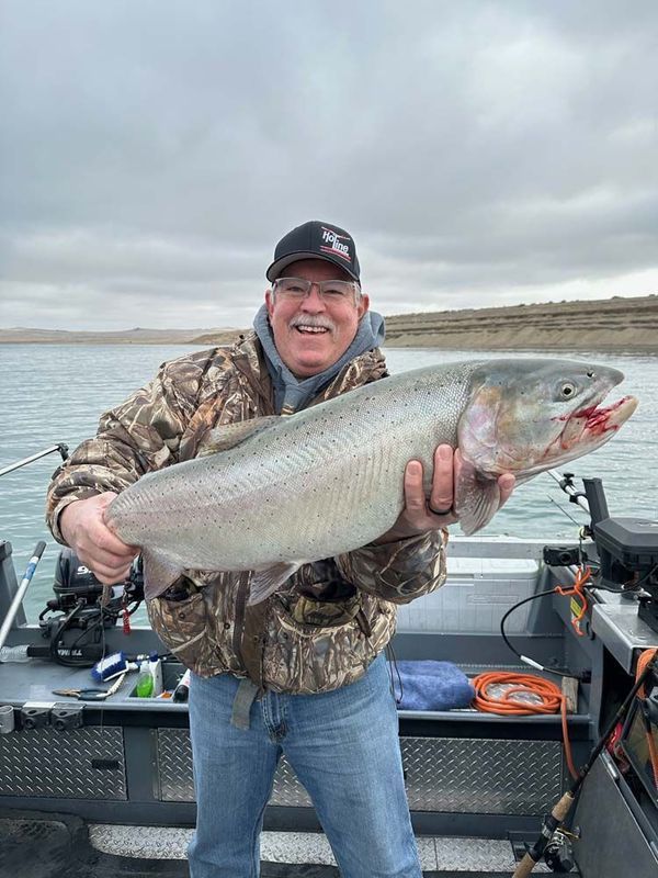 Man on boat holding large silver fish, cloudy lake background.