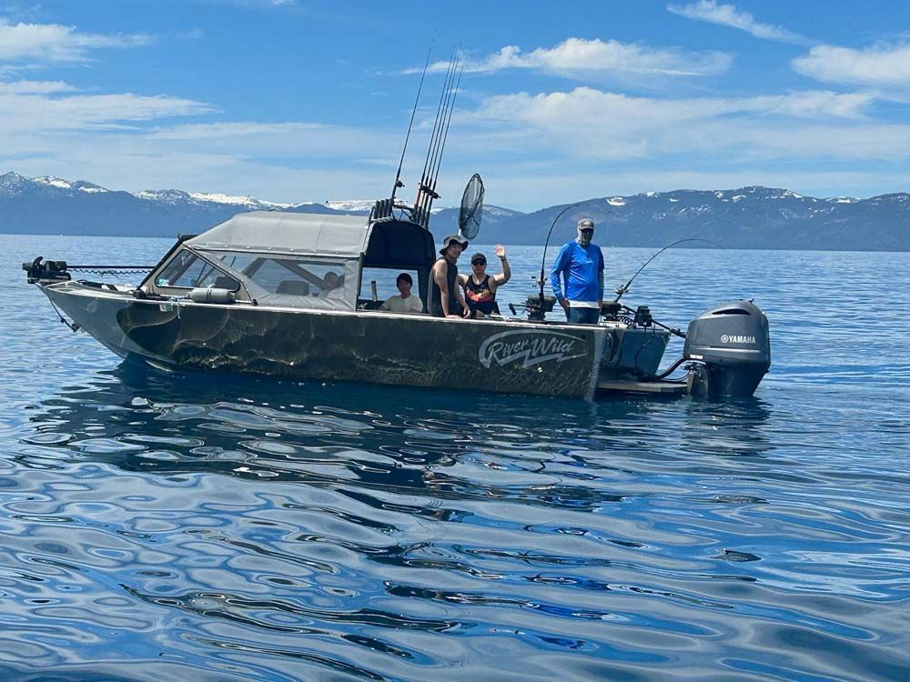 People fishing on a boat in a body of water with mountains in the background. Sunny day.