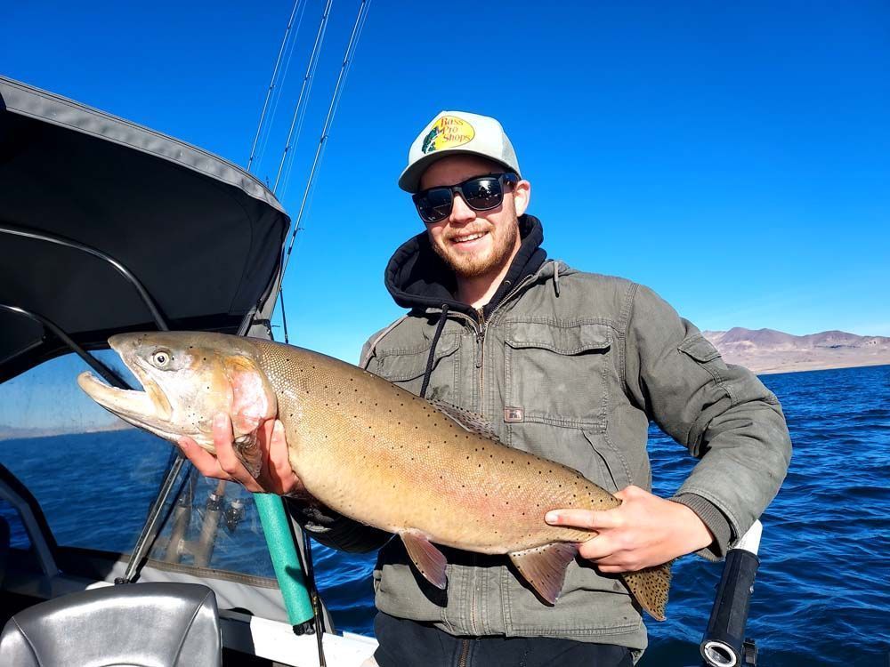 Man on a boat holds up a large fish, blue water, sunny day.