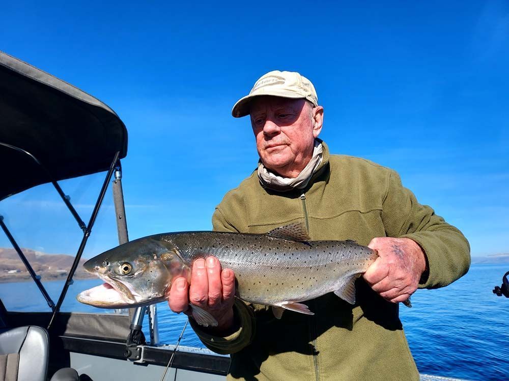 Man on a boat holding a large trout with a blue sky background.