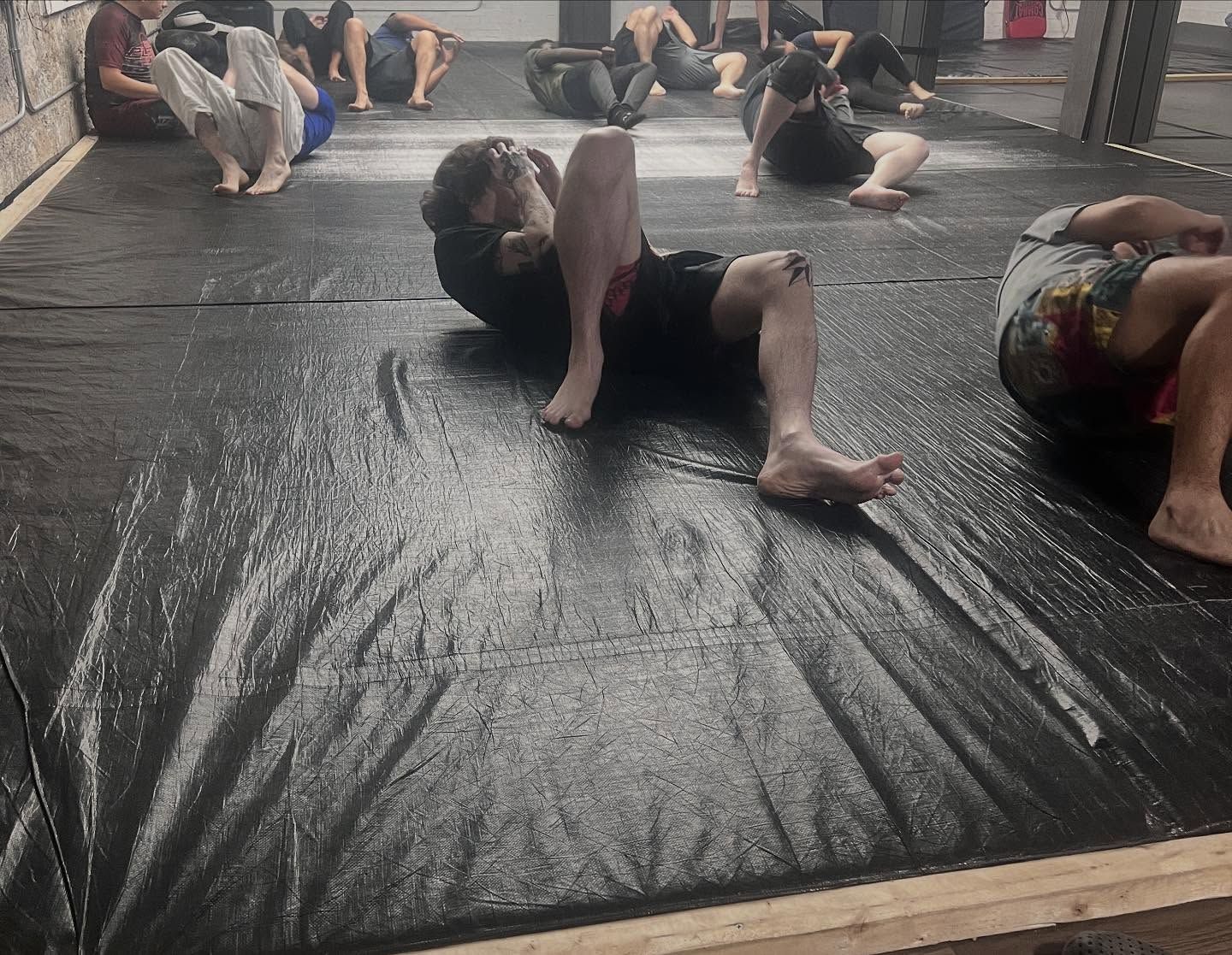 People lying on mats during a floor exercise class in a studio, stretching on a black mat.