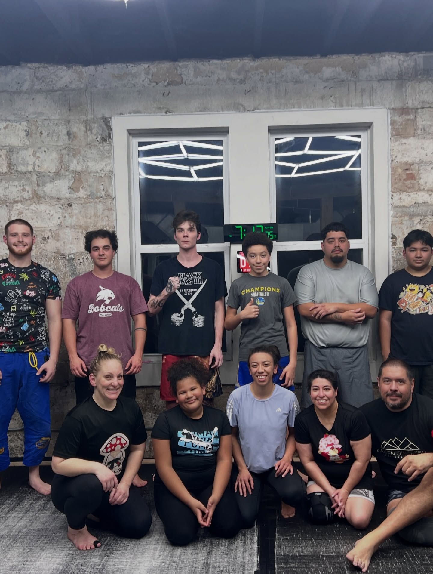 Group of people posing together in front of a stone building with a window and lights behind them.