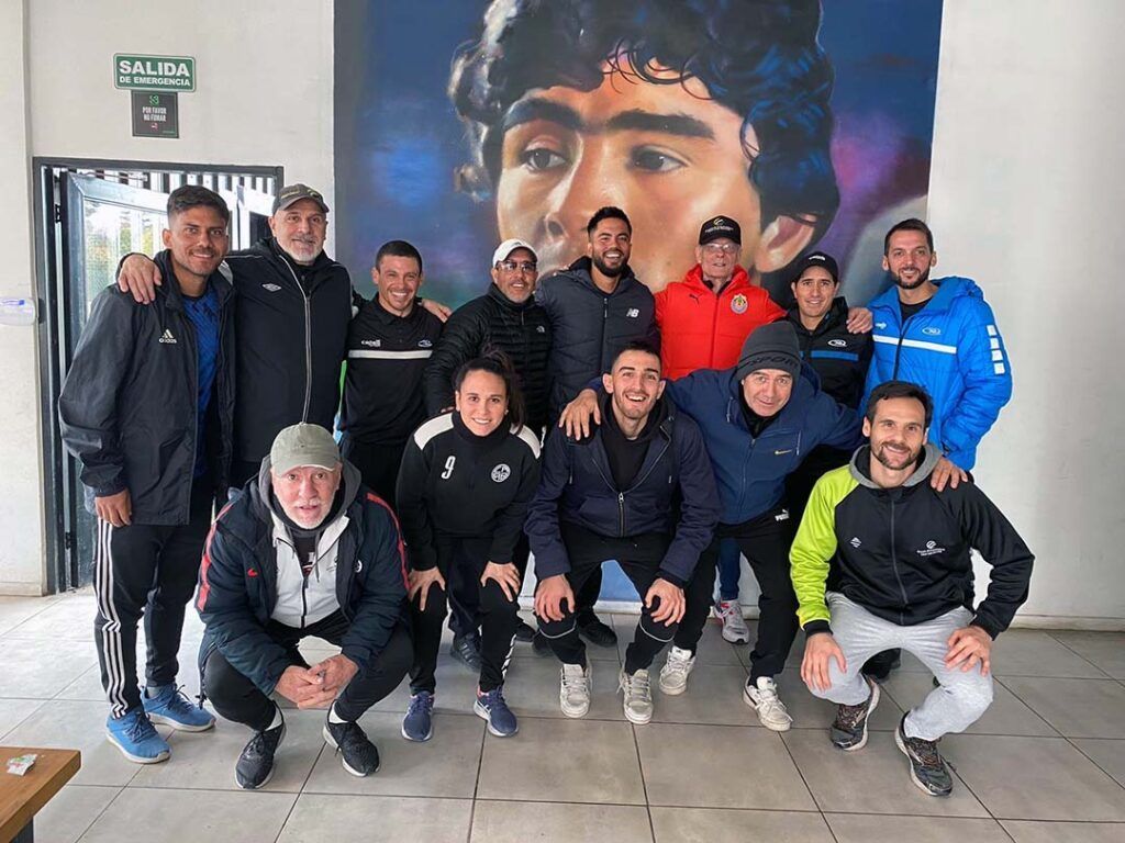 Group of people pose in front of a mural of a man; indoor setting. Some are smiling.