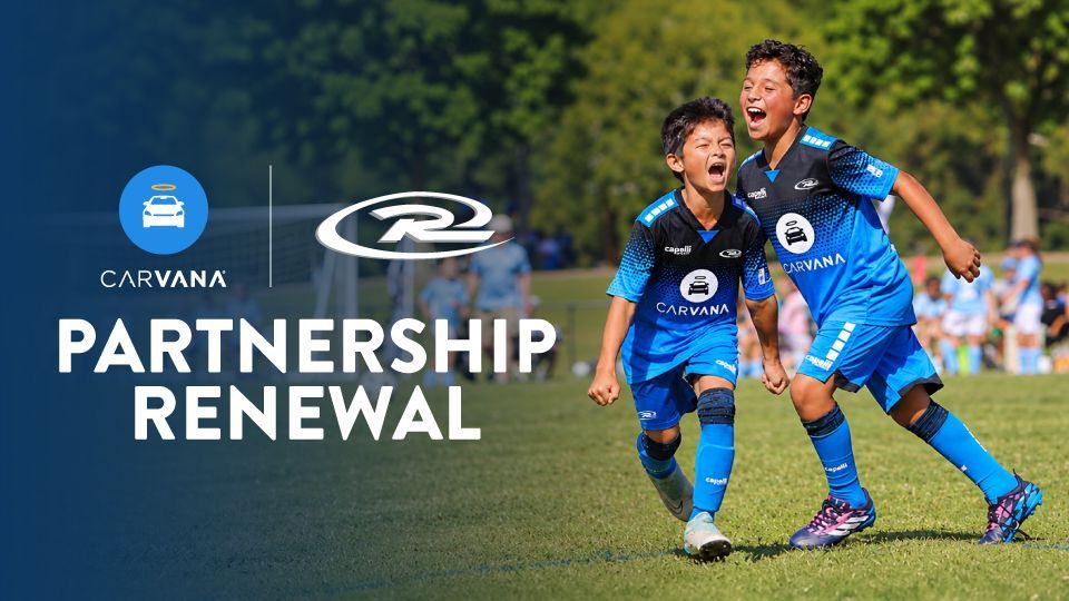 Two boys in blue soccer uniforms run and celebrate on a grassy field during a game