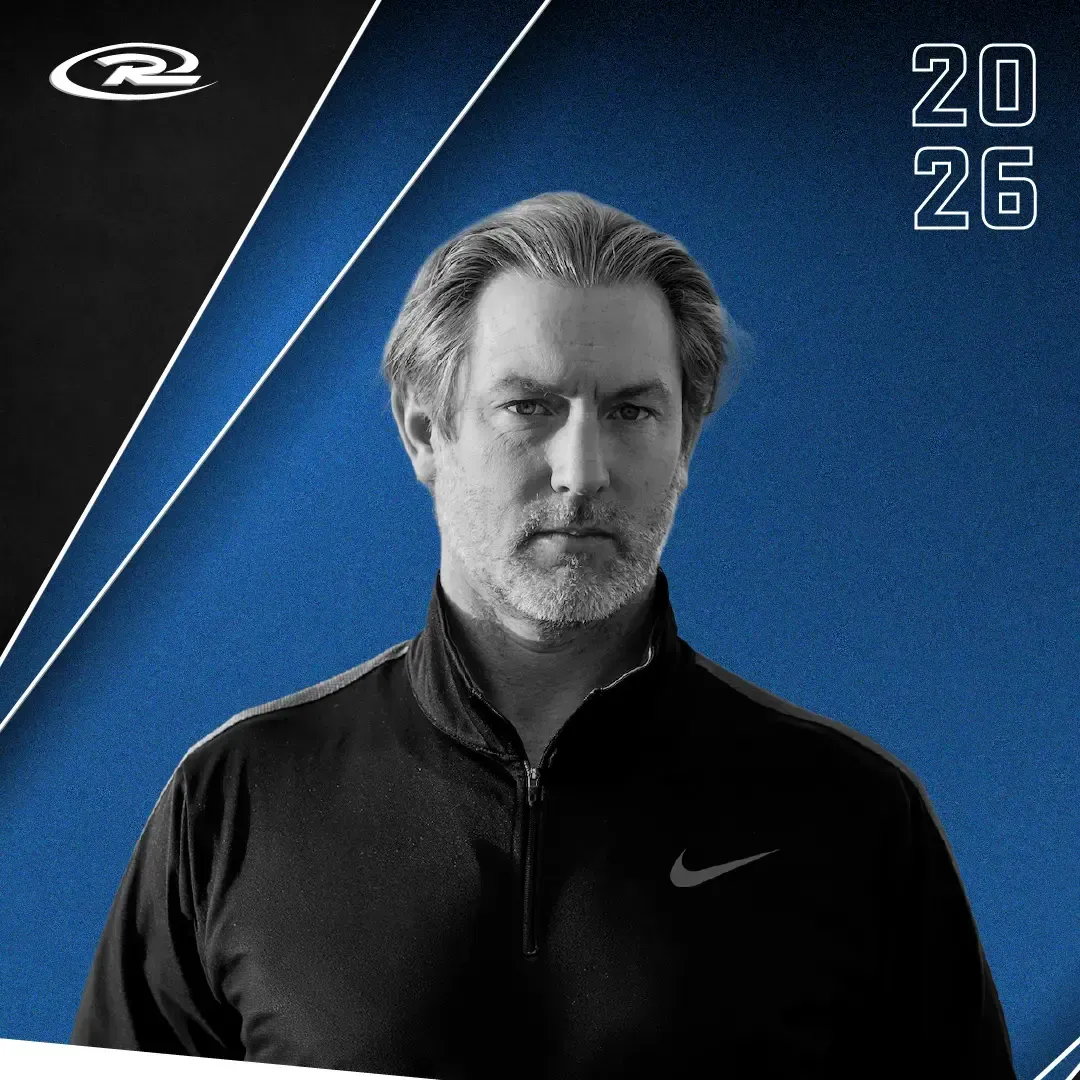 Monochrome portrait of a man in a black Nike jacket on a blue background with “2026” text