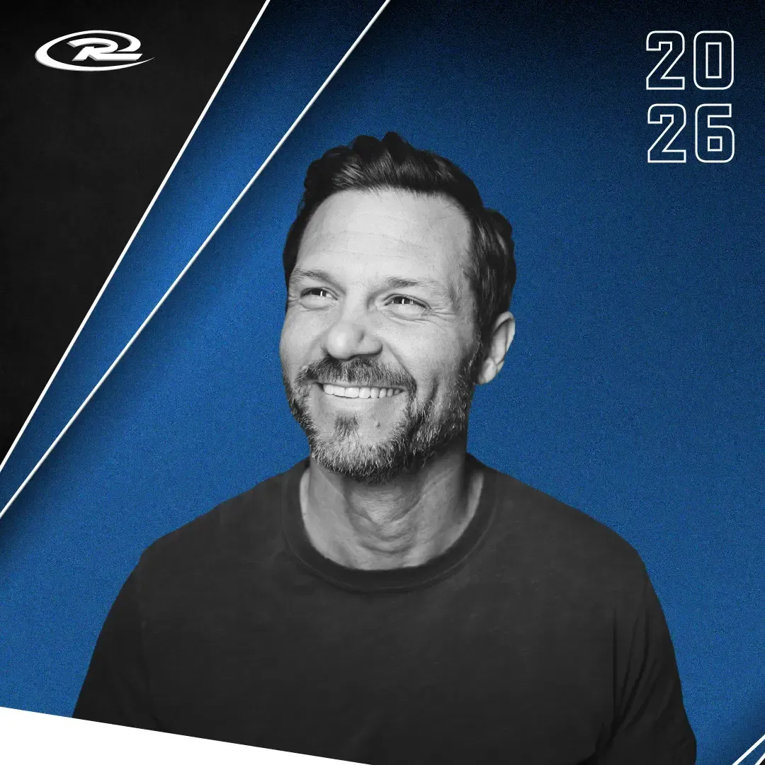 Smiling man in a black shirt on a blue background with “2026” text in the corner