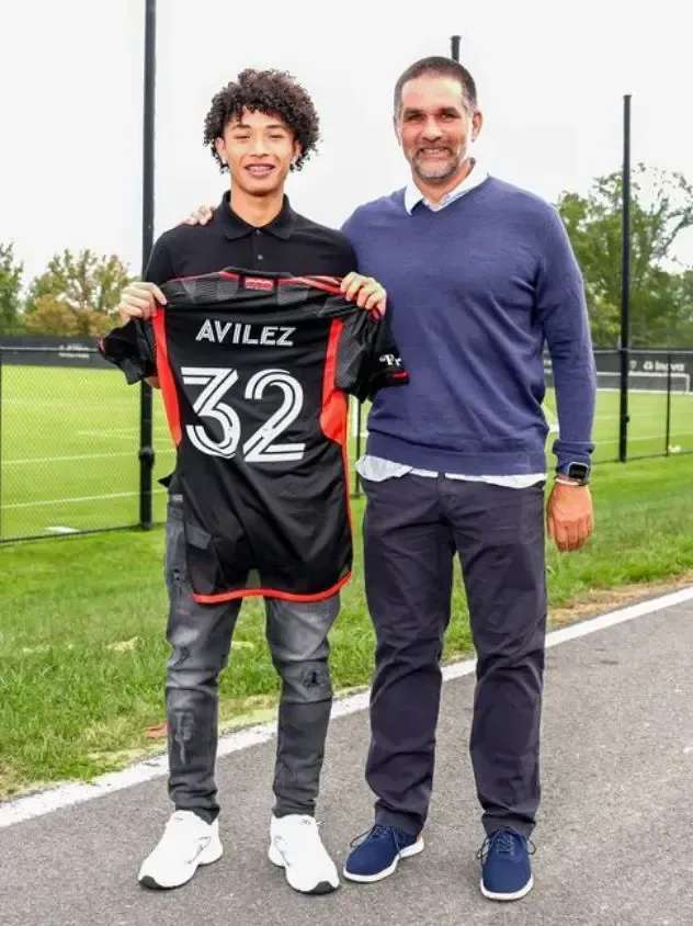 A person in a soccer jersey holds it next to another person outdoors.