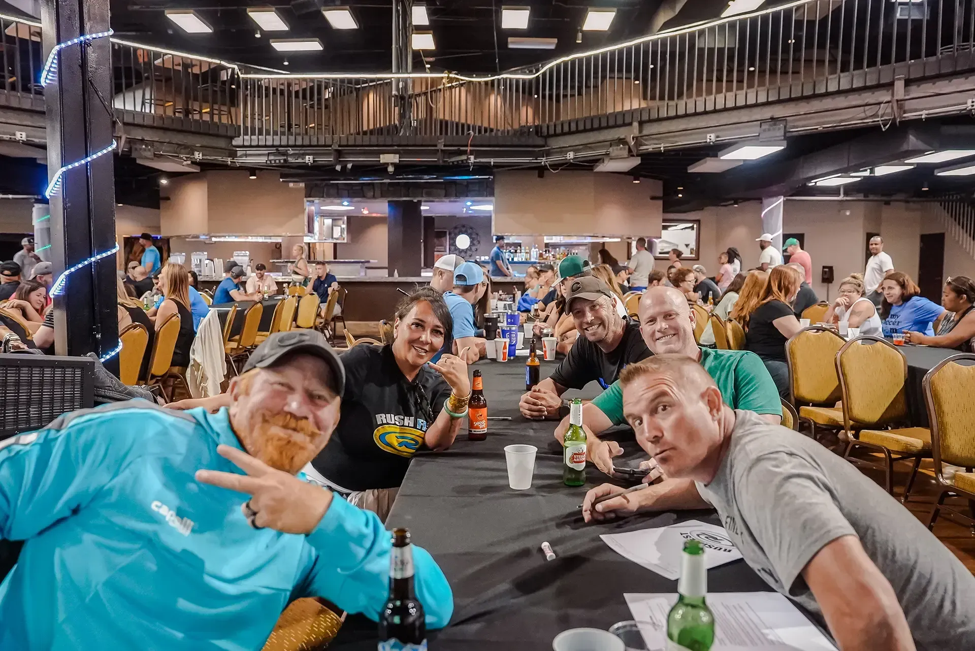 Group posing at a crowded indoor event, smiling and leaning over a table.