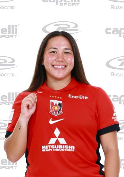 Smiling person in a red soccer jersey posing in front of a sponsor backdrop