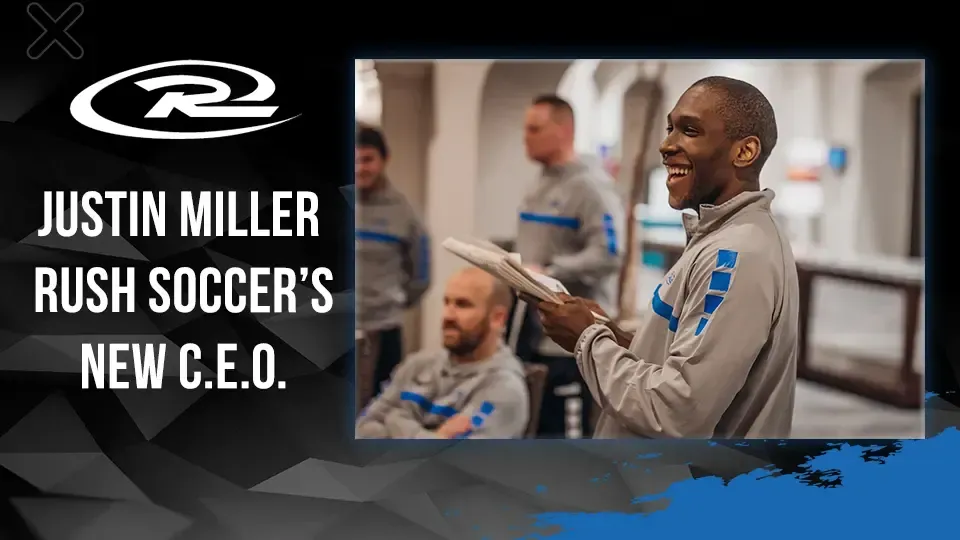 Justin Miller announced as Rush Soccer's new C.E.O. He smiles and holds a clipboard; others listen in a building.
