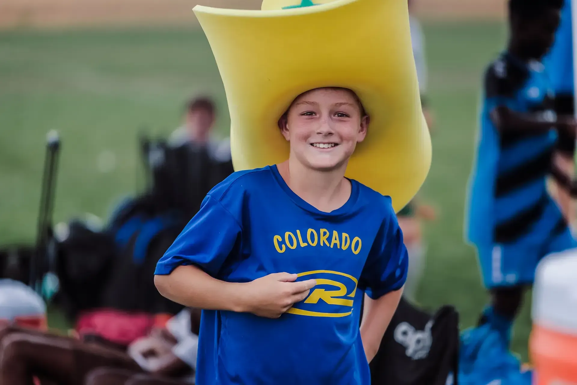 Young person smiles, wearing a large yellow hat and blue