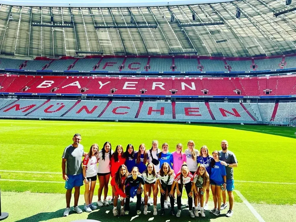 Group of people standing on a soccer field in front of a stadium that says