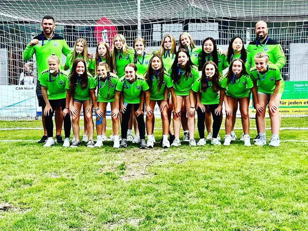 Group of people in green uniforms posing on a grassy field.