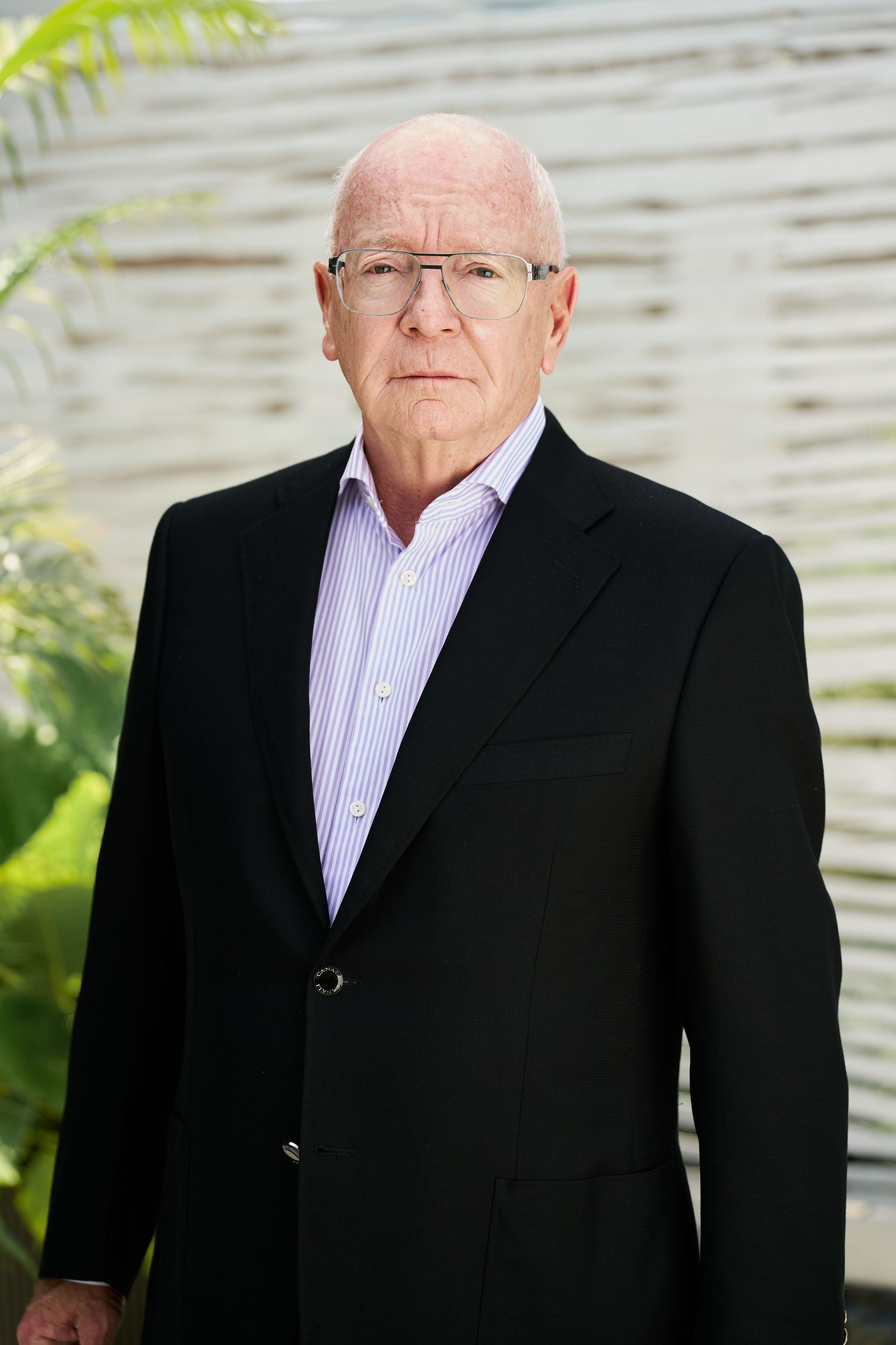 Mature man wearing glasses and a suit, standing outdoors.