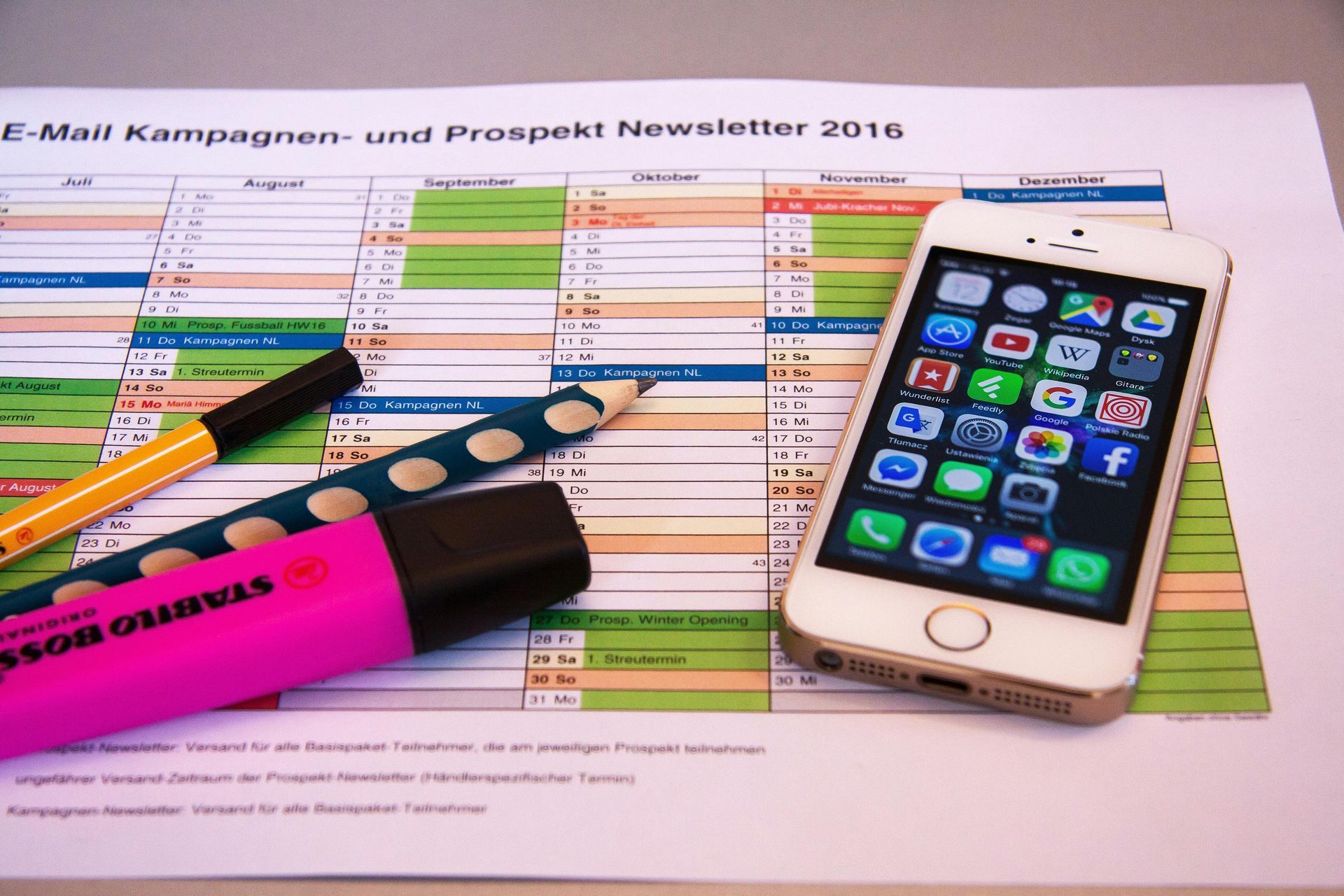 Een kalender voor 2016 met daarop een smartphone, een roze markeerstift en twee pennen.