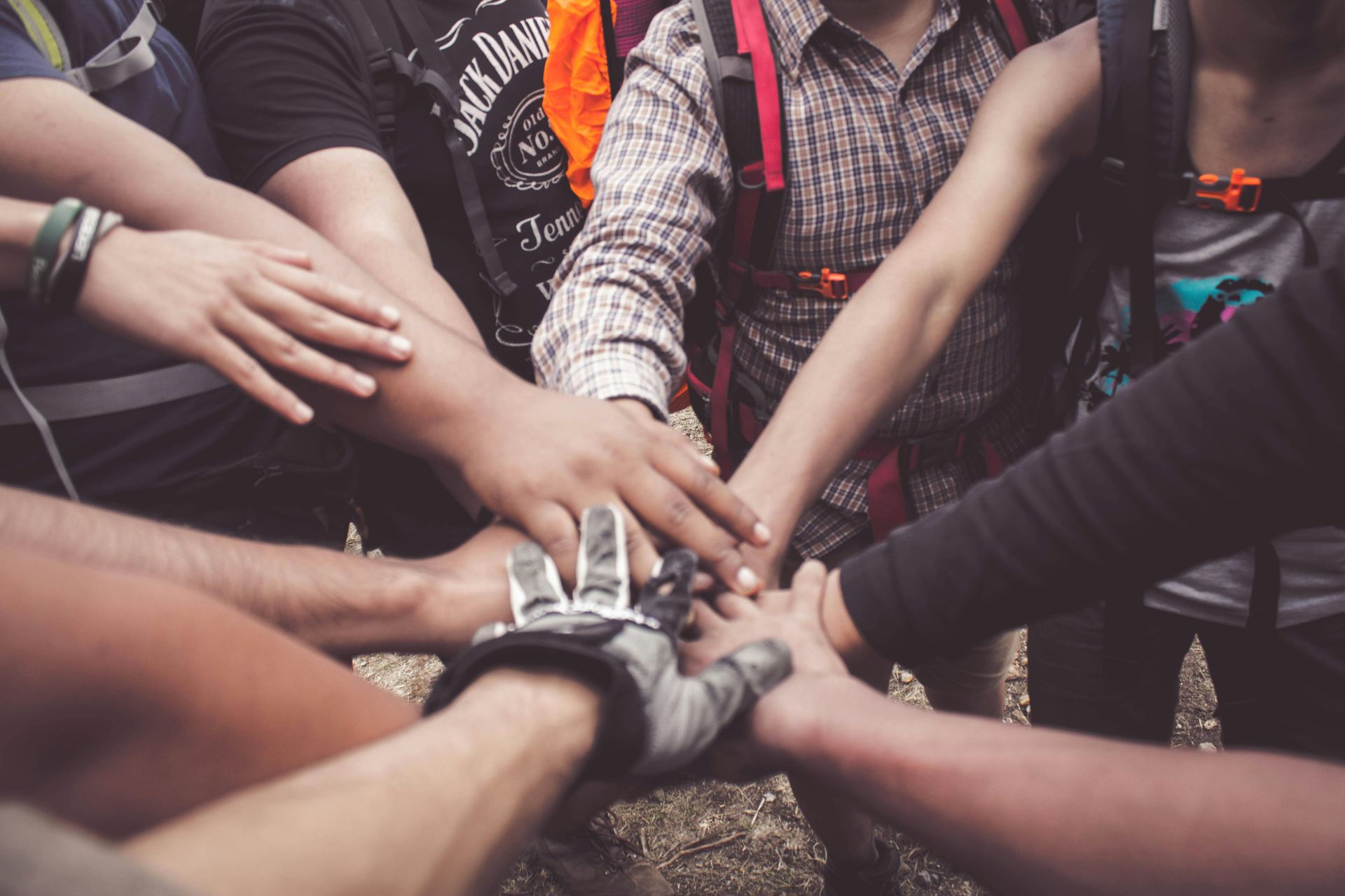 Een diverse groep mensen vormt een centrale stapel, hand in hand, gekleed in outdoor wandelkleding en rugzakken.