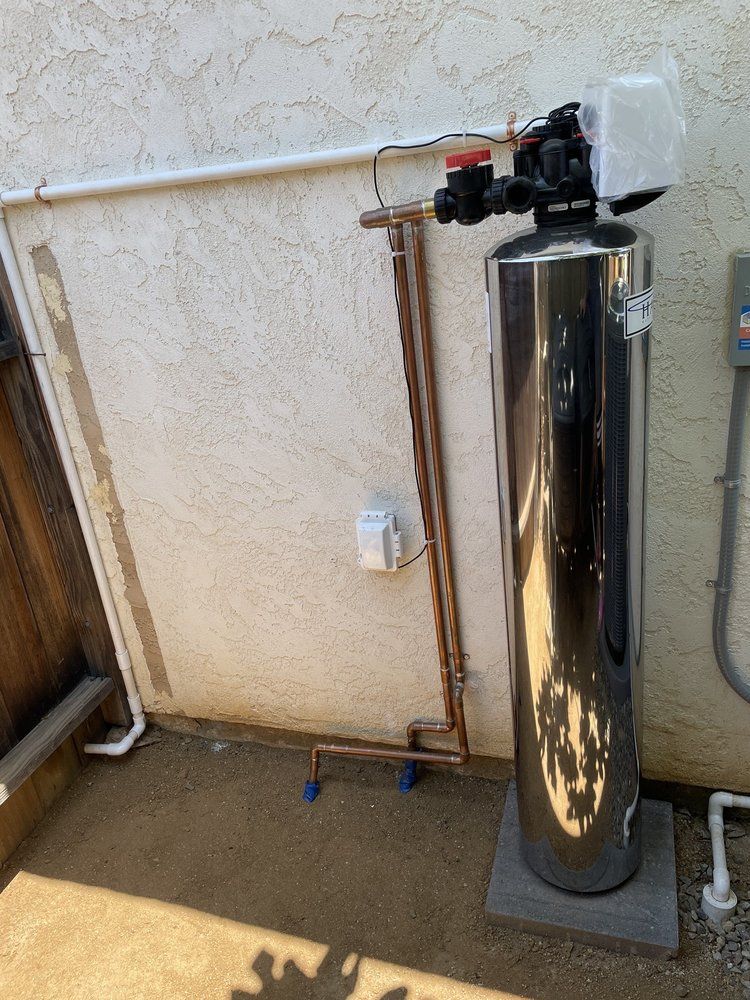 Pride Plumbing, Inc | A stainless steel water filter is sitting on the side of a building.
