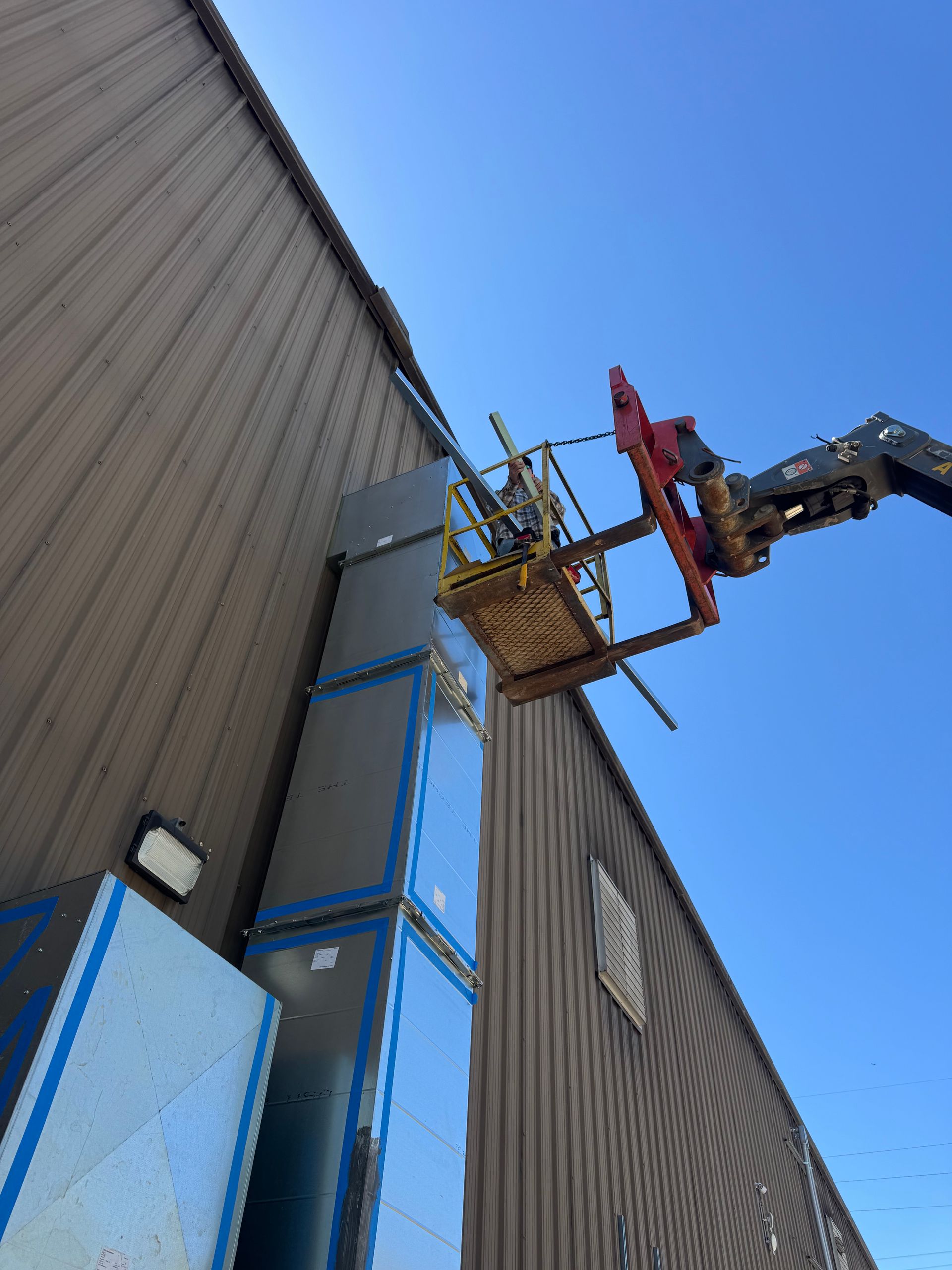 Worker on a blue lift inspecting a tall gray building exterior against a clear sky