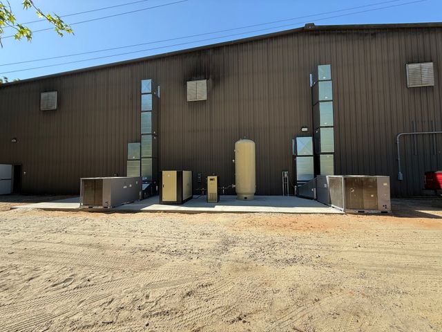Industrial building exterior with metal siding, utility doors, and HVAC units on a gravel lot.