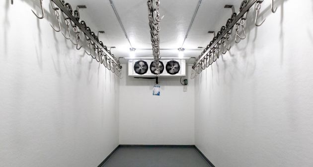 Empty white cold storage room with hanging rails and ceiling fans at the far end