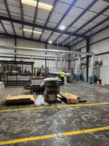 Industrial warehouse interior with stacked materials and a worker in a yellow safety vest.