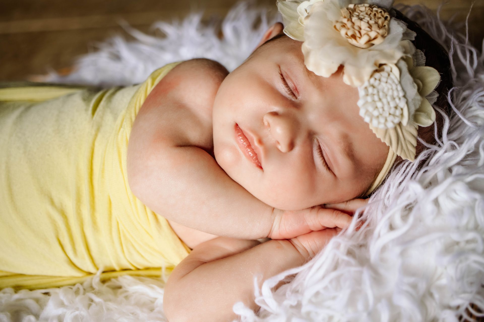A newborn baby wrapped in a yellow blanket is sleeping on a white blanket.