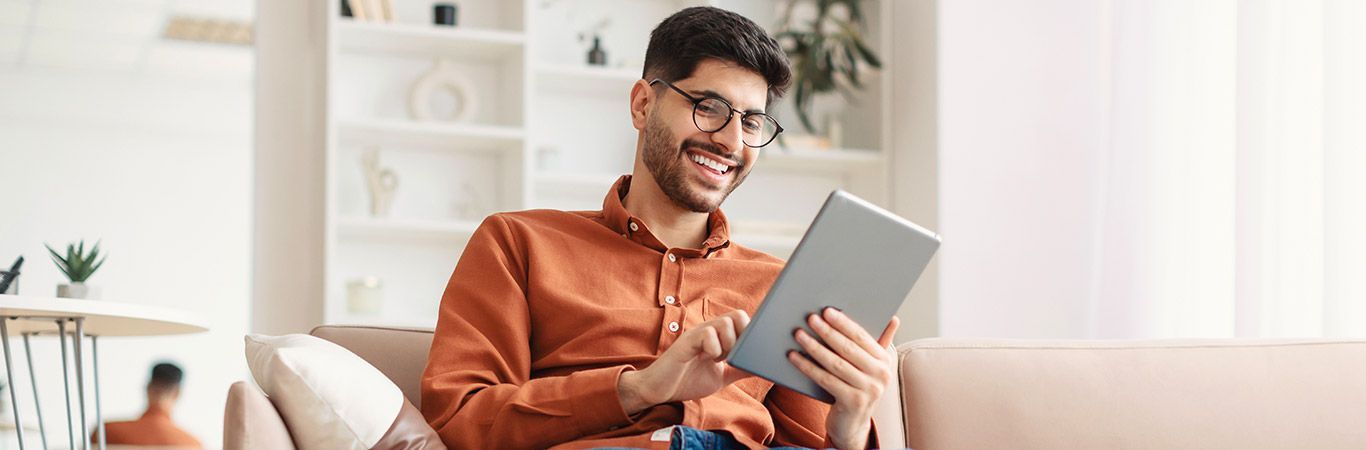 A man is sitting on a couch using a tablet computer.